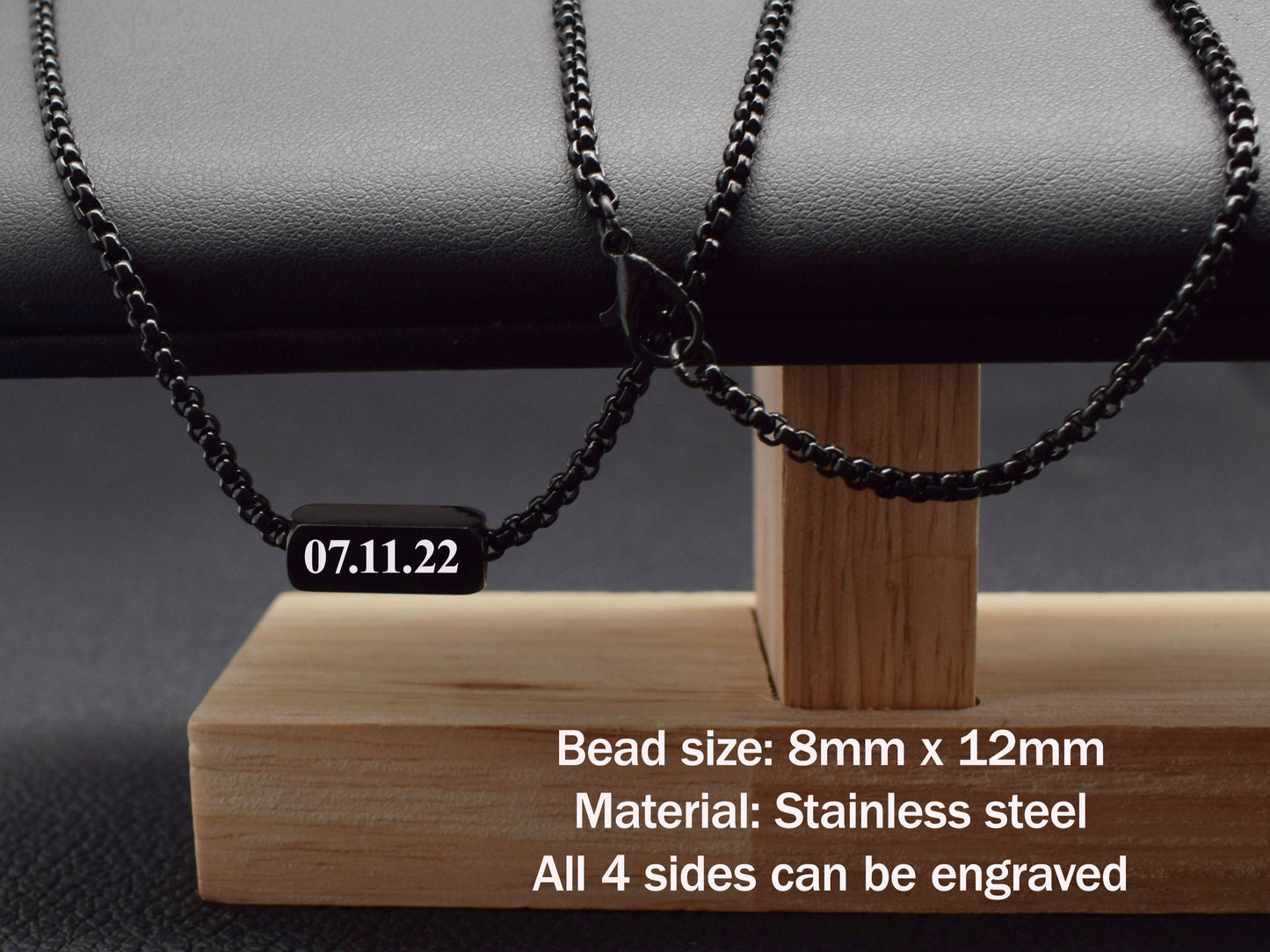 Black beaded necklace with engraved date on a wooden stand against a dark background